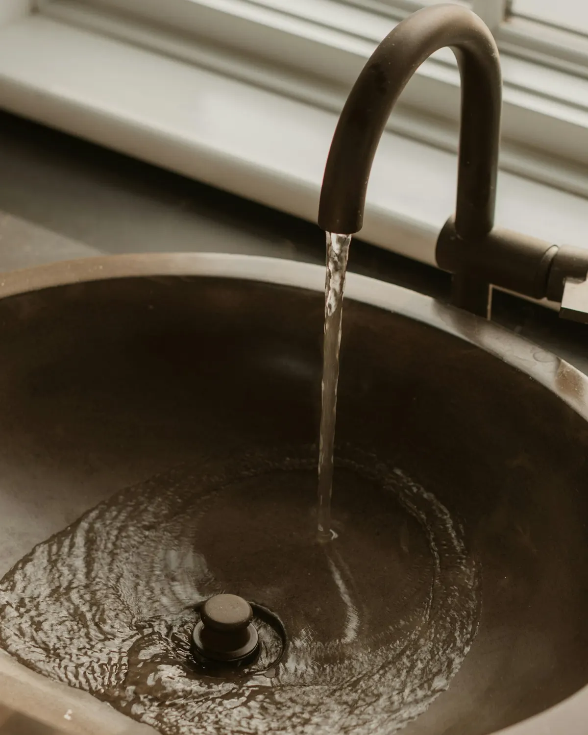 Bronskleurige kraan boven een ronde metalen waskom