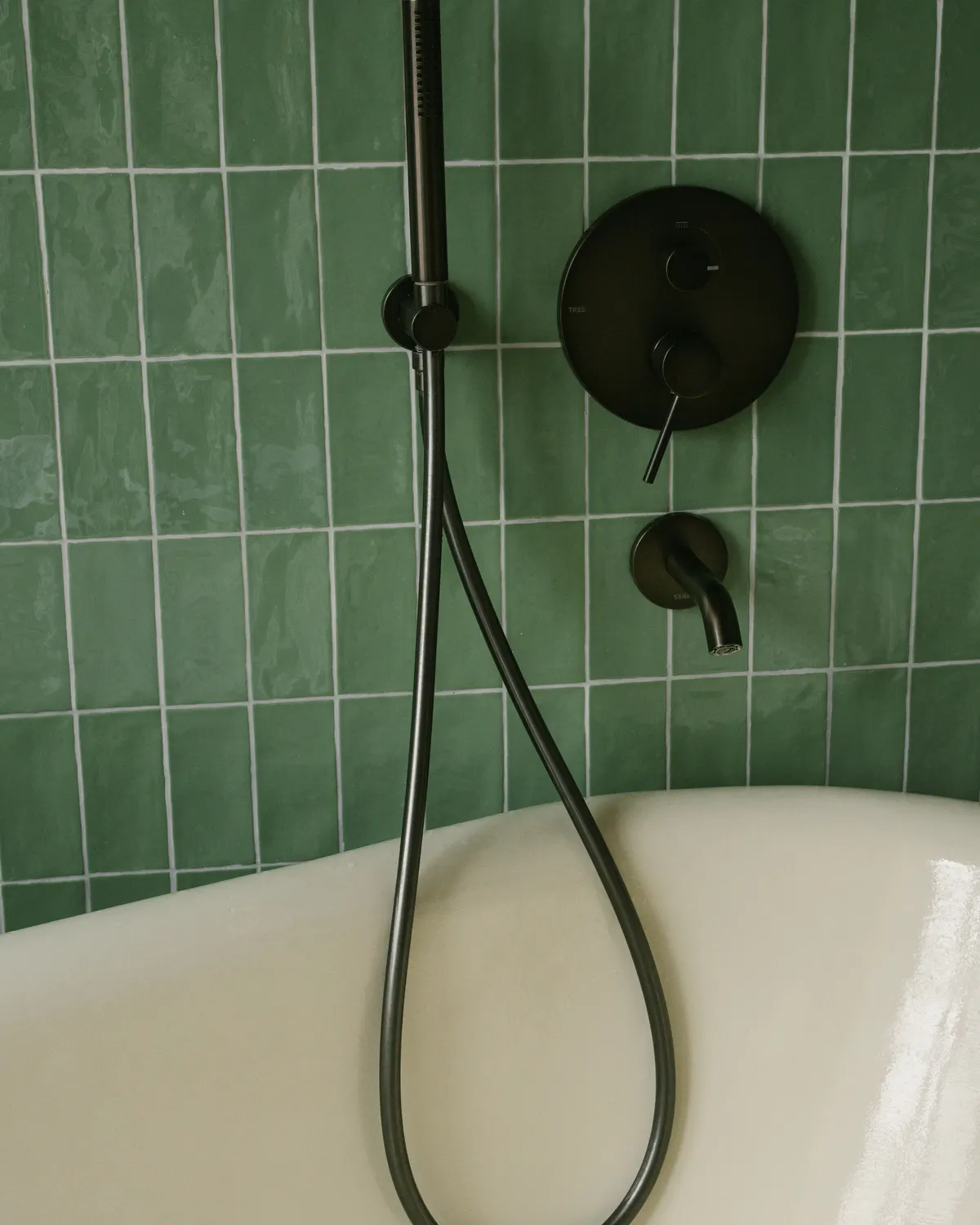 Bad voor een wand van groene geglazuurde tegels, met een zwarte handdouche