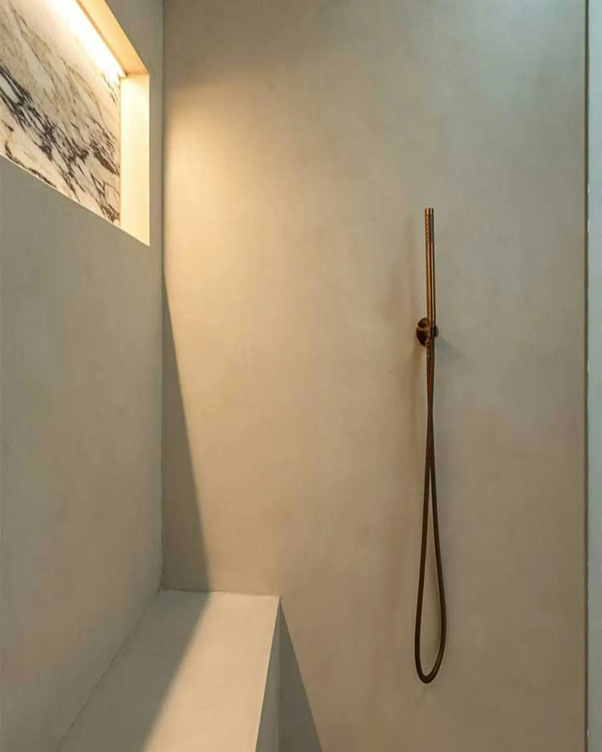 Inloopdouche in lichtgrijs microcement met een bank en een smalle handdouche