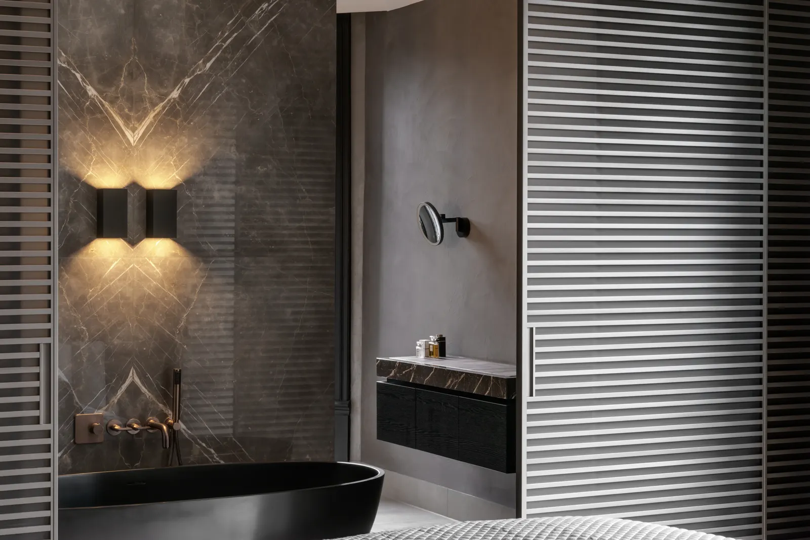 Badkamer met een mat zwart vrijstaand bad voor een wand van geaderd marmer, warm licht en gestucte wanden