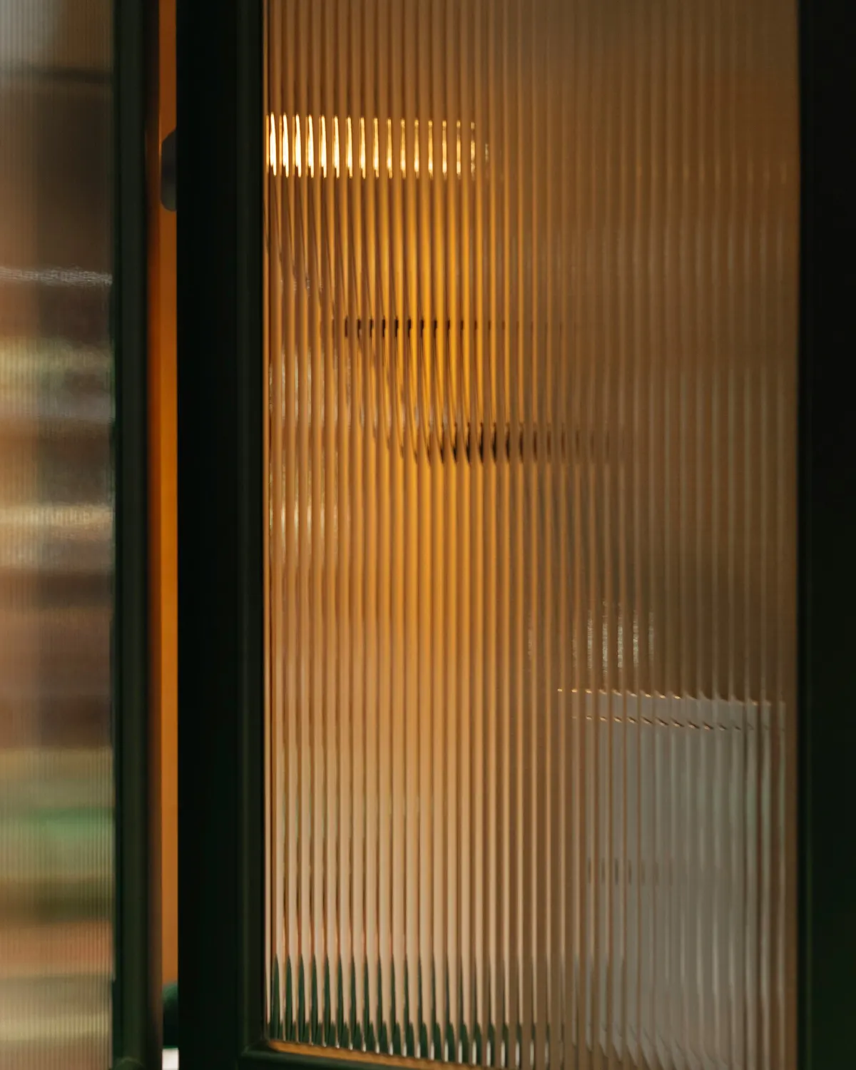 Close-up van verticaal ribbelglas in een donker kader met warm licht erachter